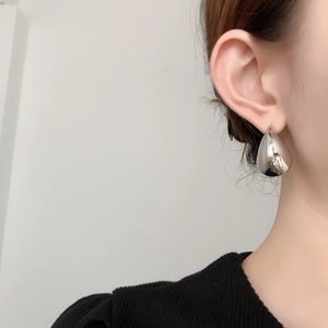 Close-up of minimalist silver water-drop earrings showing mirror finish on earlobe