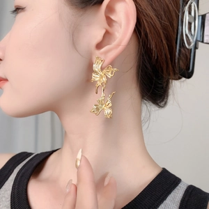 Elegant gold butterfly dangle earrings with textured metal finish on a female model