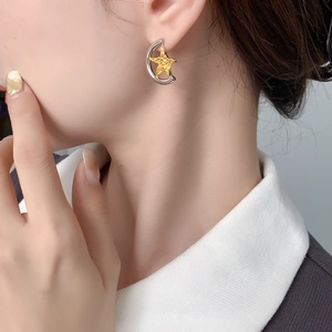 Detail of asymmetric half-moon and gold star earrings on model with metallic finish