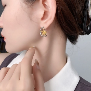 Detailed view of bicolor star and moon stud earring with hammered metal texture on ear
