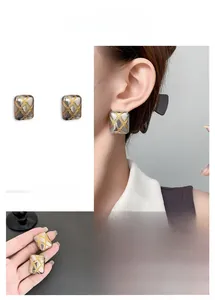 Detail of square quilted earrings with two-tone gold and silver finish on ear and hand