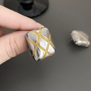 Close-up of rectangular bicolor earrings featuring golden quilted pattern on silver base