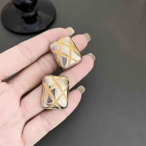 Detailed close-up of quilted two-tone gold and silver square metal stud earrings