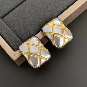 Macro detail of square quilted earrings in mixed gold and silver tones on a jewelry box