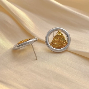 Détail de boucles d'oreilles argentées avec triangle doré texturé sur tissu satiné