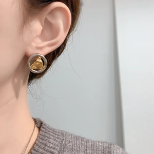 Gros plan du modèle portant des boucles d'oreilles bicolores or et argent texturées