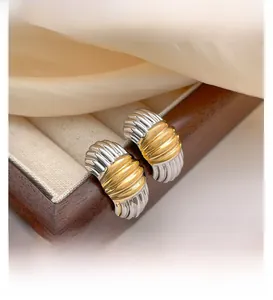 Macro shot of two-tone gold and silver striped metal earrings on a dark jewelry box