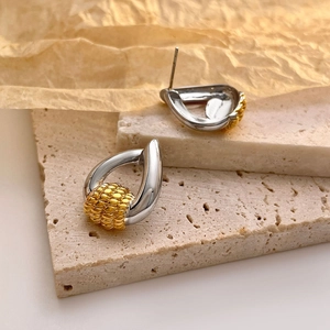 Detailed view of two-tone teardrop earrings with gold-plated grain texture on stone background