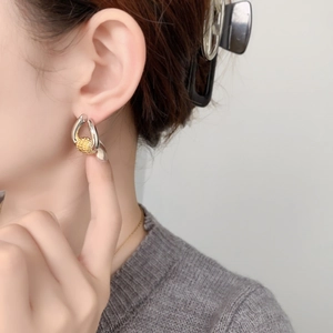 Close-up of model wearing two-tone gold and silver earrings with spherical detail