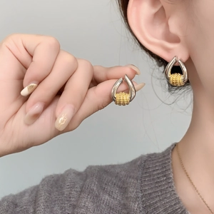 Detail of two-tone gold and silver U-shaped earrings with a textured sphere on a model