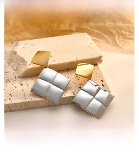 Macro shot of bicolor square stud earrings with quilted texture on beige stone