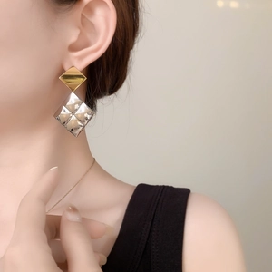 Close-up of a geometric gold and silver rhombus earring worn by a model in a minimalist style