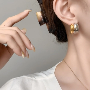 Close-up of minimalist two-tone gold and silver C-shaped earrings on a model