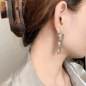 Gros plan de boucles d'oreilles pendantes fleurs argentées avec texture de pétales sur modèle