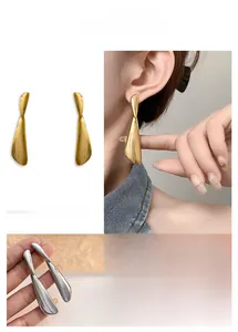 Close-up of minimalist gold and silver teardrop earrings with a polished mirror finish
