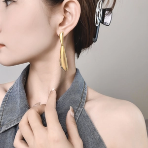 Macro view of gold drop earrings with high-gloss mirror finish worn by a model
