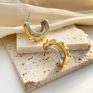 Golden C-shaped textured earrings on stone display with elegant cream silk fabric