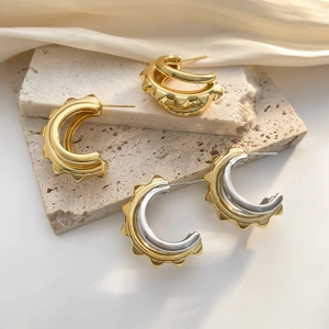 Detail of heavy industrial C-shape earrings with gear texture and gold-plated finish
