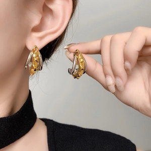 Macro shot of layered gold and silver C-shaped earrings with pyramid stud textures