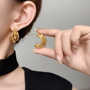 Close-up of gold-plated C-shaped earrings with industrial geometric rivet textures