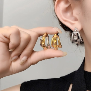 Detail of luxury gold-plated C-shape hoop earrings with pyramid studs on ear