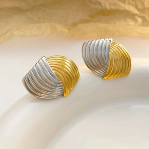 Zweifarbige fächerförmige Ohrstecker in Gold und Silber auf einem Keramiktablett