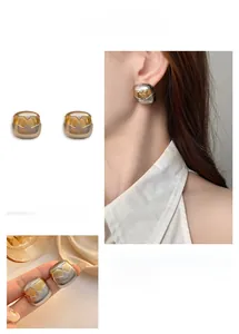 Détail de boucles d'oreilles carrées bicolores or et argent avec texture métal rainurée