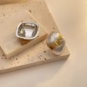 Détail de boucles d'oreilles carrées bicolores avec finitions texturées or et argent