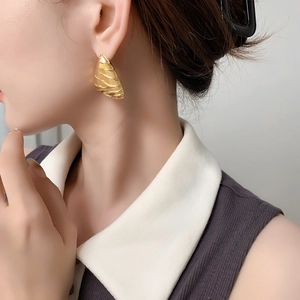 Macro detail of textured gold triangular earring with embossed waves on female model