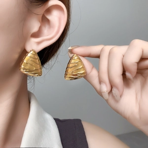 Detail of gold-plated triangular earrings with embossed irregular texture worn on ear