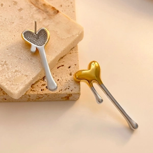 Detail of mixed-metal heart earrings with polished lava texture on stone surface