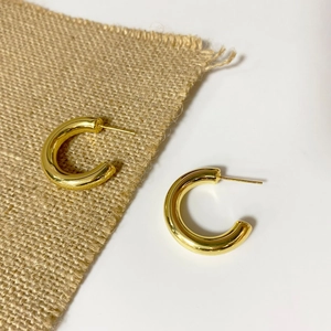 Close-up of golden hollow tube C-shaped hoop earrings with polished mirror finish surface