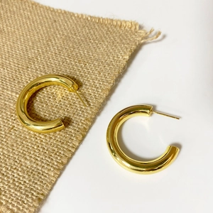 Detailed view of polished gold chunky C-shaped hoop earrings on natural jute texture