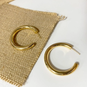 Detailed view of polished gold-finished brass hollow C-hoop earrings on a linen texture