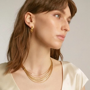 Detail of layered gold snake chain necklace and textured hoop earrings on a model