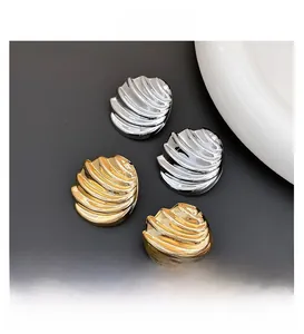 Detailed view of wave-textured shell earrings in gold and silver finishes on dark background