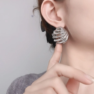 Macro detail of sculptural silver-tone wave earring with mirror finish on model
