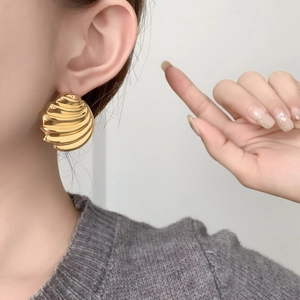 Macro detail of large gold wave seashell earrings with polished metallic surface texture