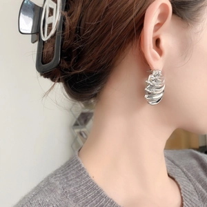 Minimalist silver wave earrings with bold shell texture shown on model in a side view