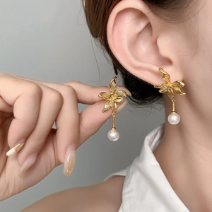 Detailed view of elegant gold orchid flower earrings with a hanging white pearl drop