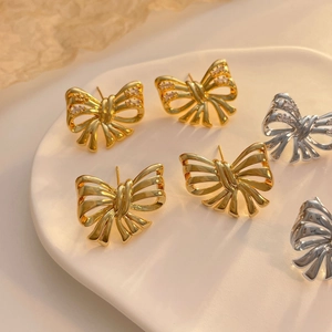 Macro shot of gold and silver bow stud earrings with zircon inlay on ceramic tray