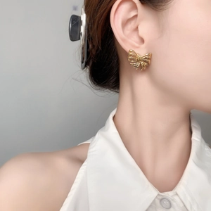 Close-up of elegant gold hollow bow earrings worn on the ear with a polished metallic finish