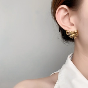 Elegant gold bow earrings with pleated metal texture worn by a model in a close-up shot