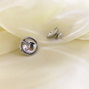 Dettaglio macro di orecchini a lobo semisferici in argento su sfondo di seta elegante