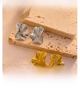 Close-up of irregular gold and silver wavy stud earrings on a beige stone base
