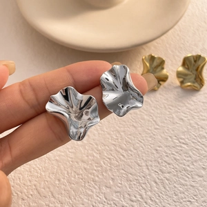 Close-up of irregular wavy metal stud earrings with polished gold and silver finish