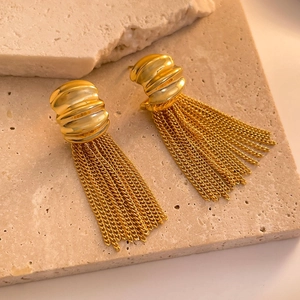 Close-up of elegant gold chain tassel earrings on a natural beige stone display