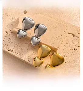 Macro shot of high-polish heart earrings in gold and silver finish on beige stone