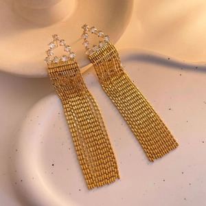 Détail de longues boucles d'oreilles à pompons dorés et zircons sur un plateau en céramique