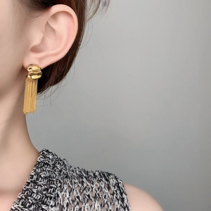 Detail of elegant gold chain tassel earrings with wavy textured stud on model